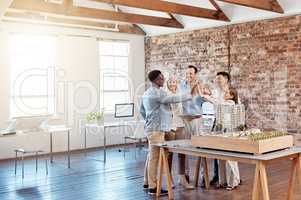 Team of happy architect engineers celebrating together with a high five after completing a small apartment complex model to scale. Group of professional designers design a blueprint office building