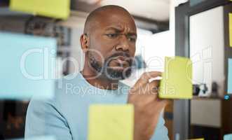 Planning is the prelude to any successful action. a businessman brainstorming with sticky notes on a glass screen.