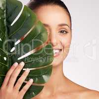Organic beauty is the way to go. an attractive young woman standing behind a plant against a studio background.