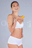 Good food choices are good investments. Studio portrait of an attractive young woman eating a tangerine against a grey background.