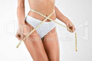 Could my waist be any smaller. a woman measuring her waist using a tape measure against a studio background.