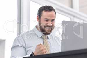 Luck is always on his side. a young businessman cheering while working on a laptop in an office.
