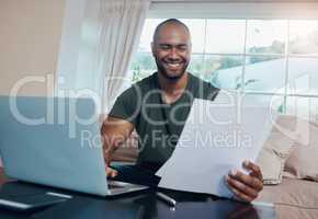 These proposals do seem compelling. a young businessman reading paperwork while working on his laptop.