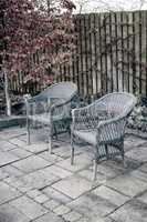 Woven armchairs outside in a rustic garden with autumn plants for relaxing after gardening. Yard landscape with two wooden chairs in nature in a backyard patio to enjoy peace and quite of winter