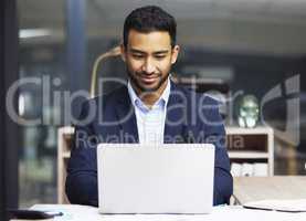 Young businessman using a laptop, trading on the stock market. Smiling trader working online with a computer and going through paperwork. Stock market and economy financial status