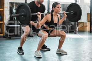 Active woman bodybuilder training and weight lifting with a personal trainer at the gym. Fit and athletic young female athlete lifts a barbell with her coach at a fitness facility