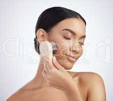 Glowing skin, count me in. Studio shot of an attractive young woman exfoliating her face with a brush against a grey background.