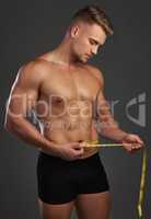 Losing weight, gaining muscles. a handsome and athletic young man measuring his waist in studio against a dark background.