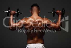 Working out those muscle groups. Rearview shot of an unrecognizable and athletic young man lifting weights while shirtless in studio against a dark background.