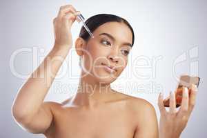 First comes retinol, then comes radiance. Studio shot of an attractive young woman using a serum on her face against a grey background.