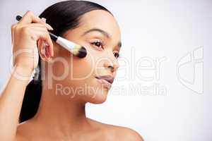 Highlighting her natural beauty a bit more. Studio shot of a beautiful young woman applying makeup to her face with a brush against a white background.