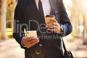 Making my way downtown. a businessman using his smartphone while drinking coffee.