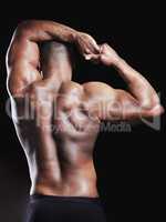 A back you wouldnt hate turning on you. Rearview studio shot of a fit young man flexing against a black background.