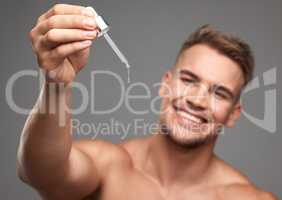 Say hello to my little friend. Studio shot of a handsome young man applying serum to his face against a grey background.