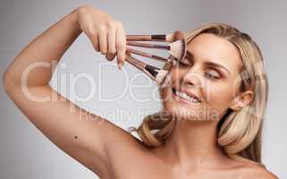 A womens greatest asset is her beauty. Studio portrait of a beautiful young woman holding a set of makeup brushes against a grey background.