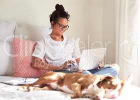 Sorry, cant, my dog wants to chill. a beautiful young woman using a laptop while relaxing with her dog in bed at home.