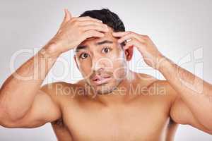 Maybe we shouldnt retouch, perhaps wrinkles are earned. Portrait of a young man checking his skin and looking concerned during his skincare routine against a grey background.