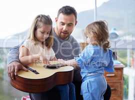 A father can teach you anything you need to know. a young father teaching his daughter to play the guitar at home.