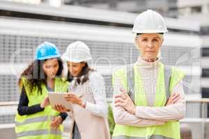 This team builds trust. Cropped portrait of an attractive mature female engineer standing with her arms folded with her colleagues in the background on a construction site.