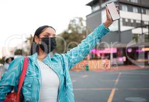 Trendy, stylish and funky student with phone travel app wearing covid mask and hailing, or waving car, taxi and local transport or lift service. Cool, fashionable and careful woman in city
