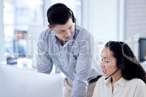 Sharing some advice on dealing with the inquiry at hand. two call centre agents working together on a computer in an office.