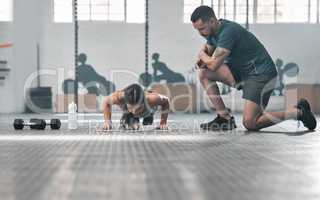 Fit and athletic woman training with her personal trainer at the gym. An active female athlete doing pushups with her coach for her morning workout routine at a fitness and exercise facility