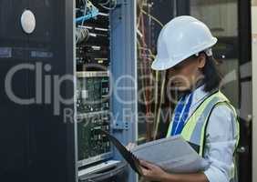 Comparing notes, taking names. a young woman working on cables in a server room.