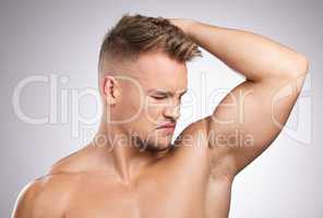 I need to be smelling fresh. a young man smelling his armpit against a grey background.