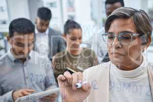 Her plans are guaranteed to work. a mature businesswoman writing notes on a glass screen while brainstorming with her colleagues in an office.