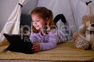 Ill be dreaming of princesses and white horses tonight. an adorable little girl using a digital tablet at night.