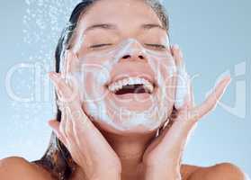 Reinvigorate, renew and restore your senses. Studio shot of a young woman washing her face while taking a shower against a blue background.