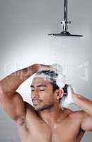 Clean hair makes him feel great. a young man washing his hair in the shower against a grey background.