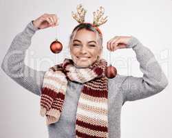 Time to decorate the tree. Studio portrait of an attractive young woman holding up baubles while dressed in Christmas-themed attire.