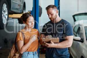 An informed auto-repair customer is a happy customer. a woman talking to a mechanic in an auto repair shop.