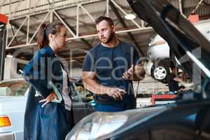 We know how to satisfy your auto needs. two mechanics working together on a car in an auto repair shop.