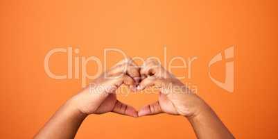 Love is all we need. an unrecognizable person showing a heart gesture against an orange background.