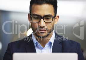 Front view of focused businessman using a laptop, trading on the stock market. Serious trader wearing glasses and working online with a computer. Stock market and economy financial status