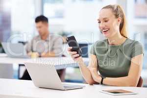 Youre never too busy for a good joke. an attractive young businesswoman sitting in the office and using her cellphone.
