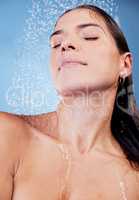 Relax, refresh, renew. Studio shot of a young woman taking a shower against a blue background.