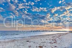 Summer sunset views on empty calm beach at low tide..Nature landscape of a coastline with a cloudy blue sky over the horizon. Seaside scene of tides and currents on a beautiful beach day