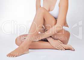 Take care of your skin. a woman sitting on the floor touching her legs against a studio background.