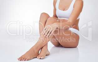 The body needs consistent upkeep. a woman sitting on the floor touching her legs against a studio background.