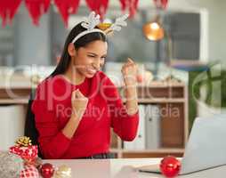 A Christmas bonus makes December even better. a young businesswoman cheering while using a laptop in a modern office at Christmas.