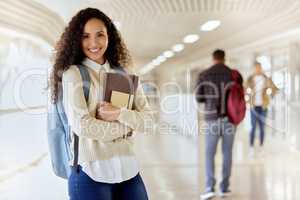 Im ready for class. Cropped portrait of an attractive young female college student standing with her textbooks in a campus hallway.