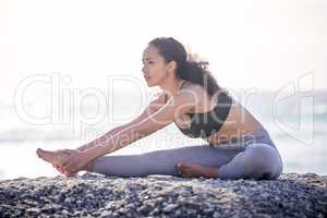 The body benefits from movement, the mind benefits from stillness. a young woman practising yoga on the beach.