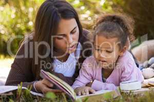 Story time in the park. Full length shot of an attractive young woman reading to her daughter while picnicking in the park.