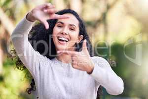 Smile, youre on candid camera. a young woman making a finger frame gesture while enjoying a day out in nature.
