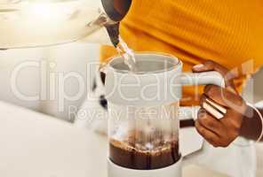 Female hands making morning coffee to enjoy with breakfast, pouring hot water from kettle in a kitchen. Closeup of casual, black woman preparing or brewing tea or espresso beverage at home.