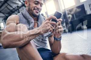 I always input my progress after a session. a muscular young man using a cellphone while taking a break from exercising in a gym.