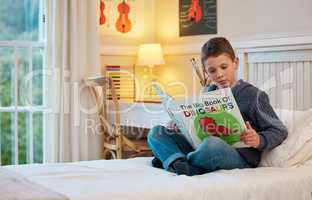 Children have a natural instinct for curiosity and discovery. a young boy reading a book about dinosaurs in a bedroom at home.